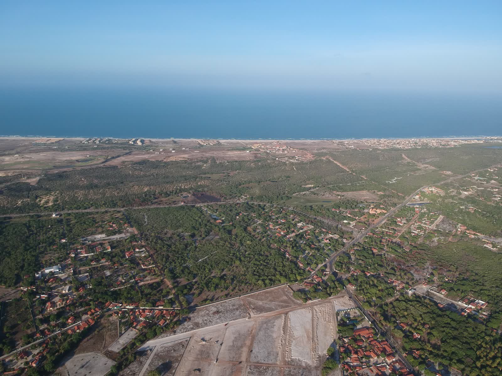 Foto aérea real da região do loteamento em Aquiraz, com a faixa de mar ao fundo