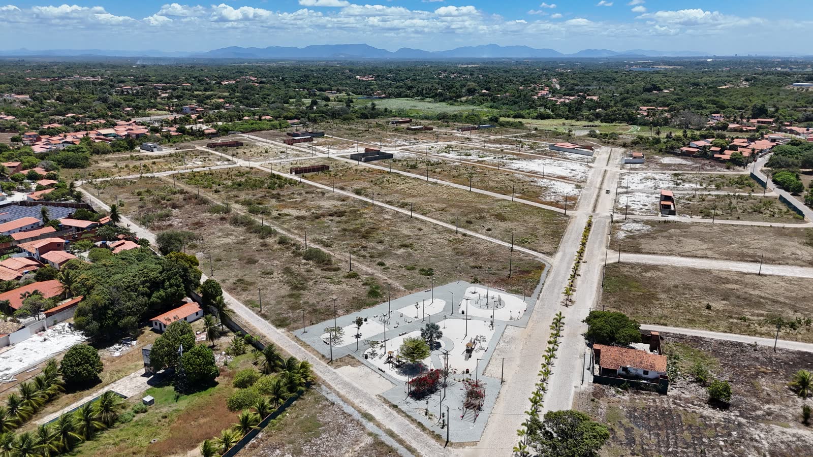 Foto aérea das ruas pavimentadas do loteamento e da praça, com a Tapera ao redor